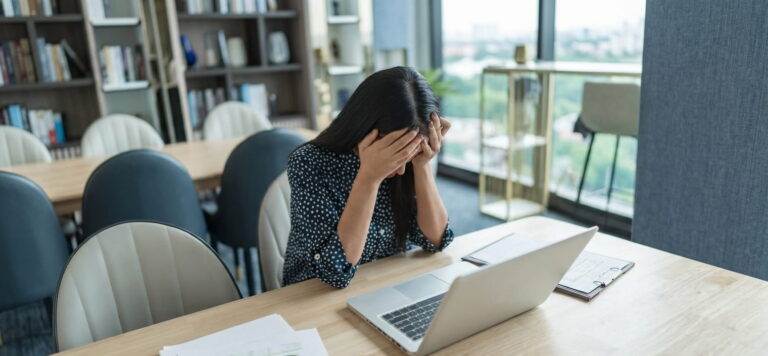 Woman experiencing stress at work while sitting at a laptop